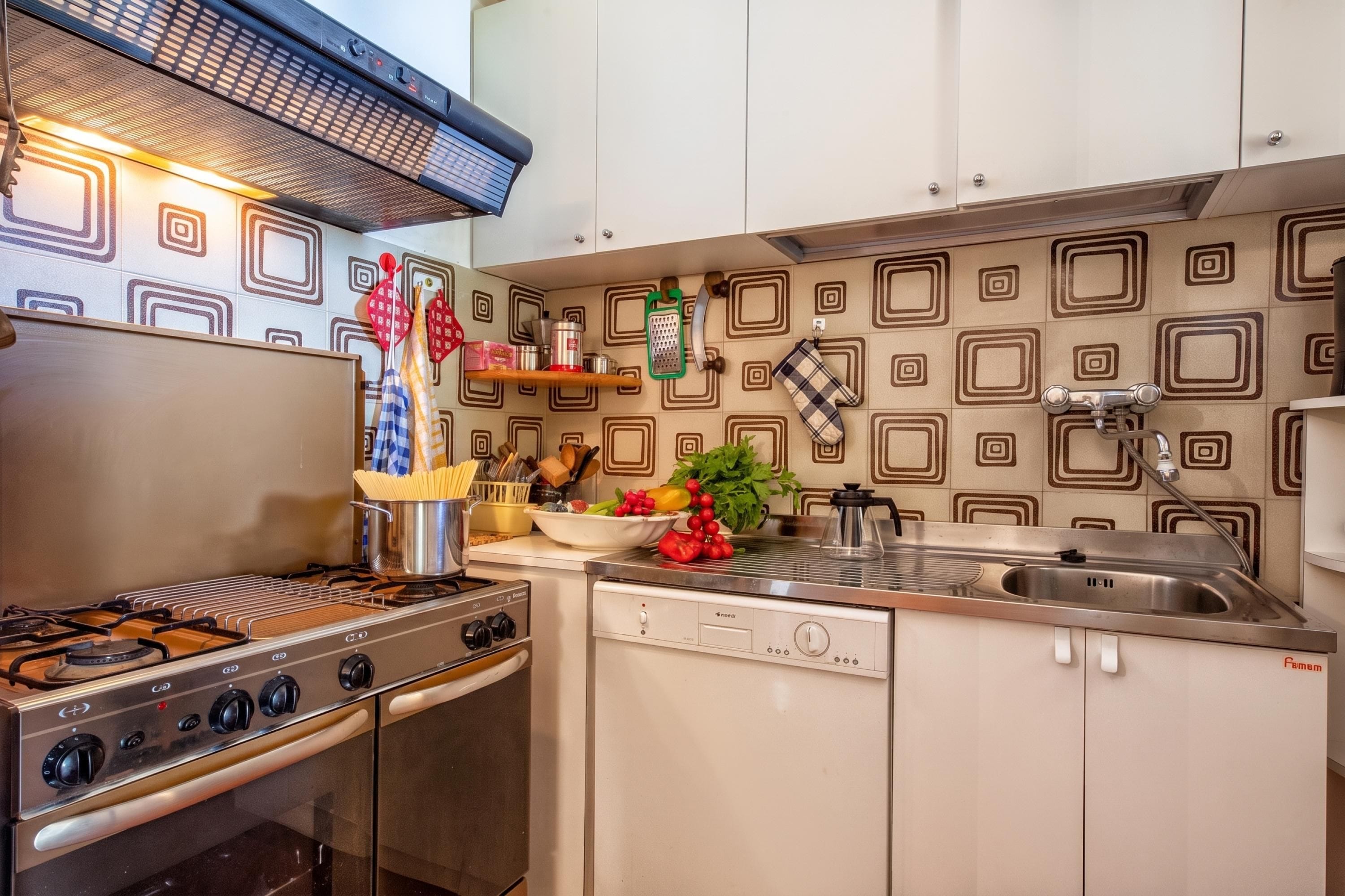 A kitchen with a gas stove, oven, and a dishwasher. There are various kitchen utensils and a bowl of fruit on the counter.