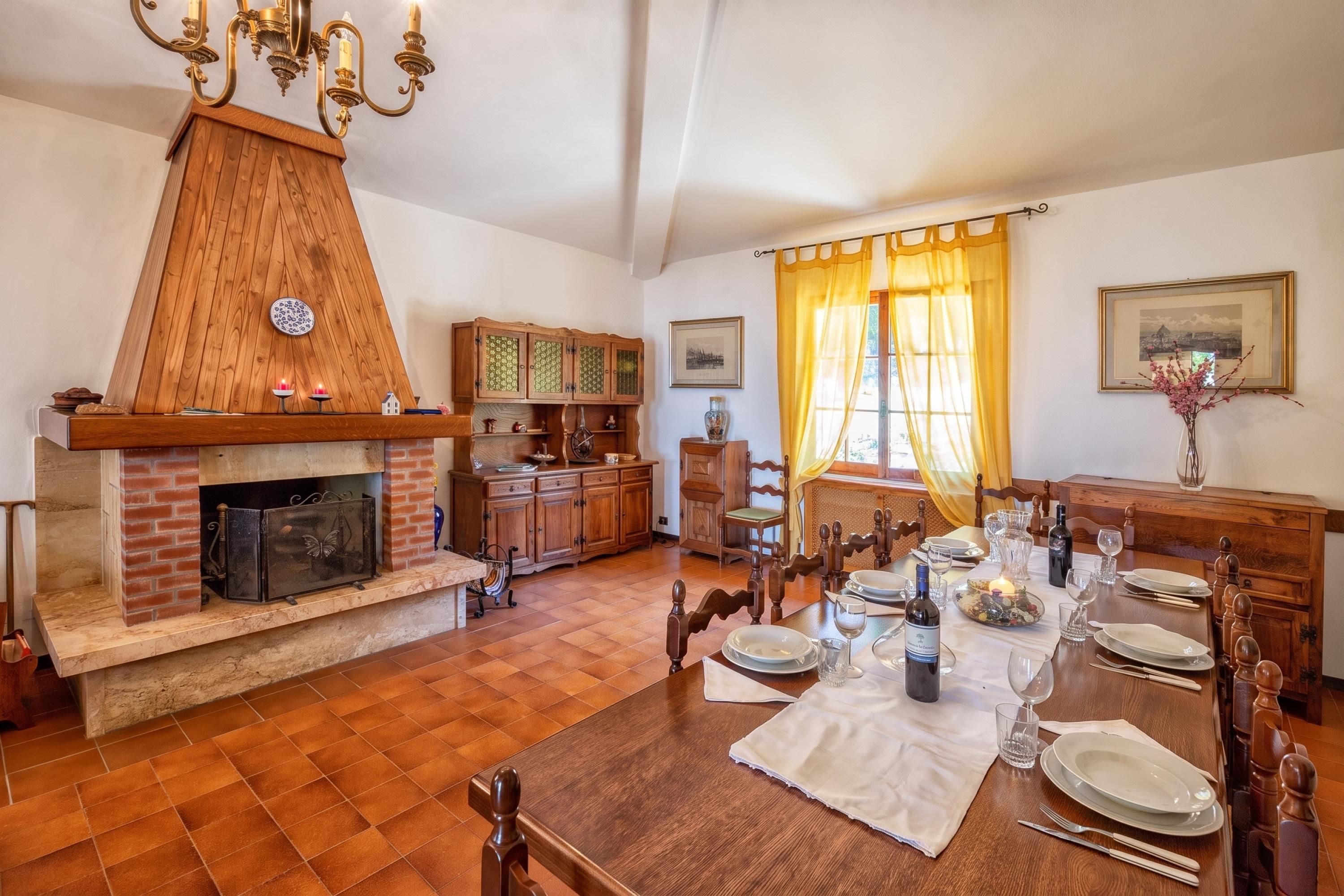 A dining area with a wooden table set for a meal, a fireplace, and a dining room with a window and curtains.