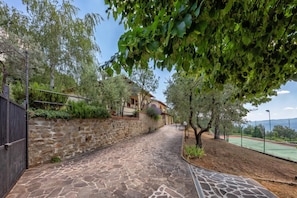 A stone pathway leading to a building with a stone wall and a fenced tennis court. - Tuscany Apt Marco Private Pool&Tennis 6, Loro Ciuffenna, Italy (Loro Ciuffenna)