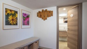 Un passadís amb una banca, dues fotografies florals emmarcades, una decoració mural de fusta i un bany visible per una porta oberta.