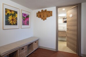 Un passadís amb una banca, dues fotografies florals emmarcades, una decoració mural de fusta i un bany visible per una porta oberta.