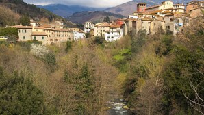 Un poble de vessant amb edificis de pedra tradicionals, un tros de riu i muntanyes al fons.