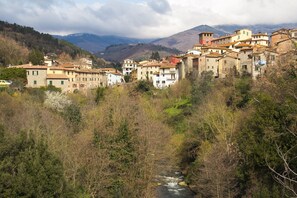 Un poble de vessant amb edificis de pedra tradicionals, un tros de riu i muntanyes al fons.