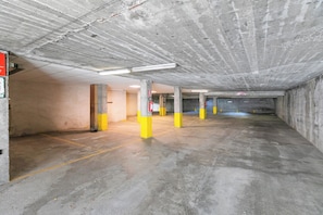 A parking garage with concrete pillars, fluorescent lighting, and a fire extinguisher.