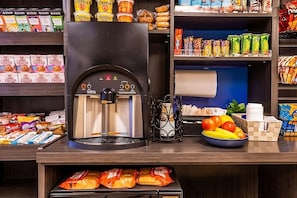 Eine Selbstbedienungs-Getränkestation mit Kaffeeautomat, Snacks und frischem Obst.