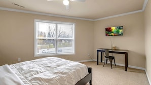 Ein Schlafzimmer mit Bett, Schreibtisch, Stuhl, Deckenventilator und einem Fenster mit Jalousien.