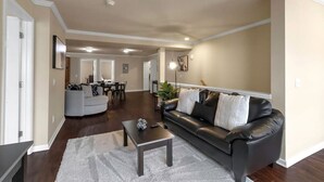 Ein geräumiges Wohnzimmer mit grauem Sofa, einem Couchtisch und einem Essbereich im Hintergrund.
