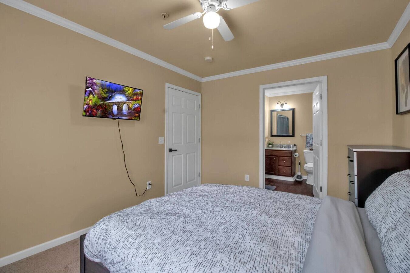 Ein Schlafzimmer mit Bett, Deckenventilator, Fernseher, Badezimmer mit Waschbecken und Spiegel sowie einer Tür.