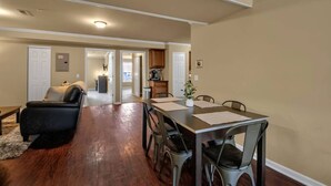 Un vaste espace de vie comprenant une table à manger, des chaises et un canapé en cuir. Au fond, on aperçoit une cuisine avec des placards et un plan de travail.