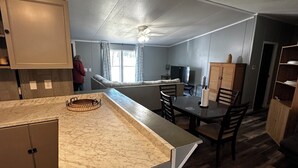 Una cocina con encimera de mármol, armarios de madera, una zona de comedor con sillas y un ventilador de techo.
