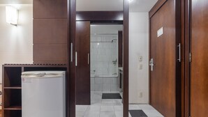 A hotel room with a wooden wardrobe, a white refrigerator, and a shower area visible through a glass door. - Leoncio 706 in S o Paulo (São Paulo)