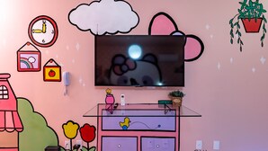 Habitación decorada en tonos rosados, con una televisión, un teléfono y una planta pequeña en la pared.