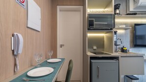 A compact kitchen with a microwave, stove, and sink. A dining table with plates and cutlery is set. - Melo Alves 32 2p 1q (São Paulo)
