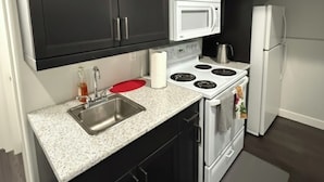 A compact kitchen with dark cabinets, a white microwave, a stove, and a refrigerator. - RR Luxury Basement Suite, located in a peaceful and friendly neighborhood (Brandon)