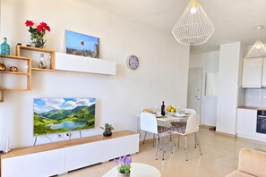A modern living room with a dining area, a mounted clock, and a large landscape painting. - Sea Vista Apartment 158, Durres, Albania (Durres)