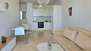 A modern kitchen with white cabinets, a dining area with a white table and chairs, and a beige sofa in a living area. - Sea Vista Apartment 158, Durres, Albania (Durres)