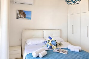 A hotel room with a bed, a nightstand, a wardrobe, a wall-mounted air conditioner, a framed picture, and a bouquet of flowers. - Sea Vista Apartment 158, Durres, Albania (Durres)