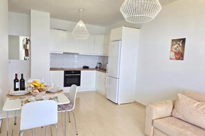 A modern kitchen with white cabinets, a dining area with a table set for two, and a beige sofa. - Sea Vista Apartment 158, Durres, Albania (Durres)