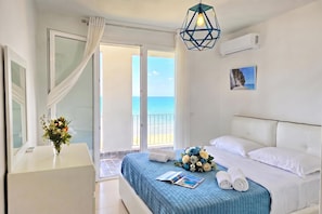 A hotel room with a bed, a bedside table with a vase of flowers, a view of the sea through a glass door, and a painting on the wall. - Sea Vista Apartment 158, Durres, Albania (Durres)