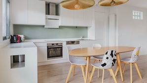 A modern kitchen with white cabinetry, a built-in oven, and a dining area with a wooden table and chairs. - Blueground | Chaillot, city view, nr Eiffel Tower (Paris)