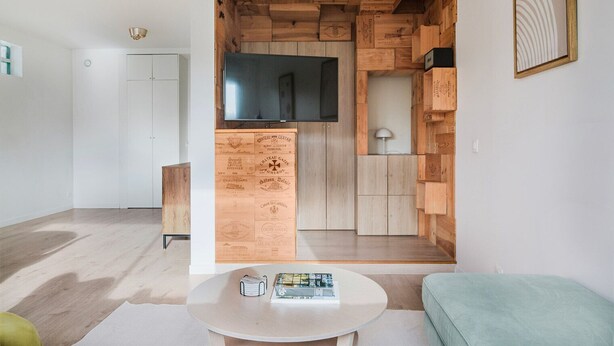 A modern living room with a wooden wall unit, a flat-screen TV, a round white table, and a green sofa. - Blueground | Chaillot, city view, nr Eiffel Tower (Paris)