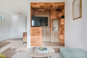 A modern living room with a wooden wall unit, a flat-screen TV, a round white table, and a green sofa. - Blueground | Chaillot, city view, nr Eiffel Tower (Paris)