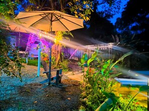 An outdoor garden area with a large umbrella, a wooden bench, and a variety of plants. - Sloth Villa (San Ramón)