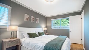 A bedroom with a bed, nightstands, a window with blinds, and wall art.