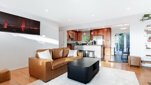 A modern living room with a brown leather sofa, a black coffee table, and a large painting of a bridge.
