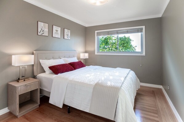 Un dormitorio con cama, mesitas de noche, una ventana y decoración en la pared.
