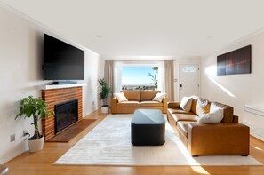 Una sala de estar moderna con un televisor de pantalla plana, chimenea, un conjunto de sofás y un amplio ventanal con vistas a la ciudad.