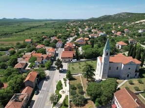 An aerial view of a town with a prominent church featuring a tall spire, surrounded by residential buildings with red-tiled roofs. - The Grandfather Villa Heated Pool Retreat (Stankovci)