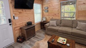 A cozy cabin interior with a wooden interior, a sofa, a coffee table, and a television mounted on the wall. - Peaceful 2BR cabin between Montgomery & Troy, AL with trails and stocked pond (Ramer)