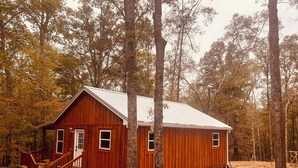 A wooden cabin with a porch and a staircase, surrounded by trees. - Peaceful 2BR cabin between Montgomery & Troy, AL with trails and stocked pond (Ramer)
