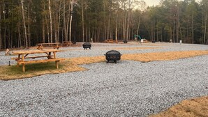 A campground with picnic tables, fire pits, and a gravel parking area surrounded by trees. - Peaceful 2BR cabin between Montgomery & Troy, AL with trails and stocked pond (Ramer)