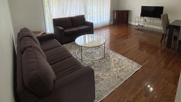 A living room with a dark brown sofa, a glass coffee table, and a flat-screen TV on a stand. - Cozy Home in North York Toronto (Toronto)