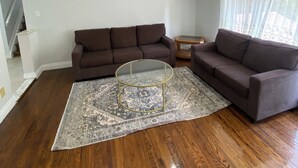 A living room with a brown sofa, a glass coffee table, and a patterned rug on wooden flooring. - Cozy Home in North York Toronto (Toronto)