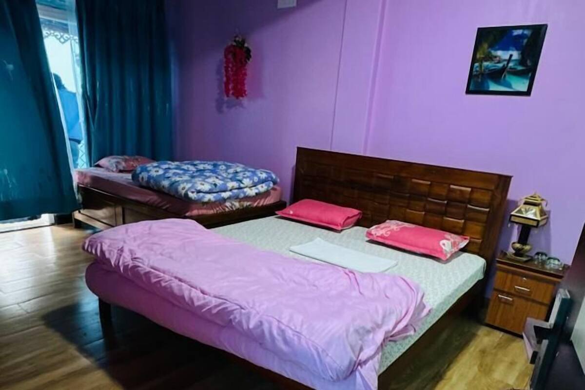 Une chambre avec deux lits, un plancher en bois, une tête de lit en bois, une table de chevet et une lampe fixée au mur.
