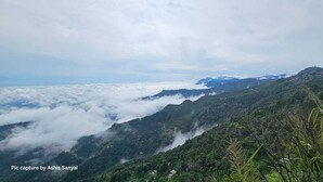 Paisaje montañoso con vista a un valle, rodeado de vegetación y algunos edificios.