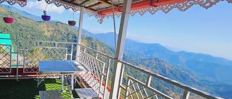 A terrace with a table and chairs, overlooking a mountainous landscape.