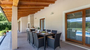 Um pátio externo com pérgola de madeira, mesa de jantar posta com pratos, copos e uma tigela de frutas.