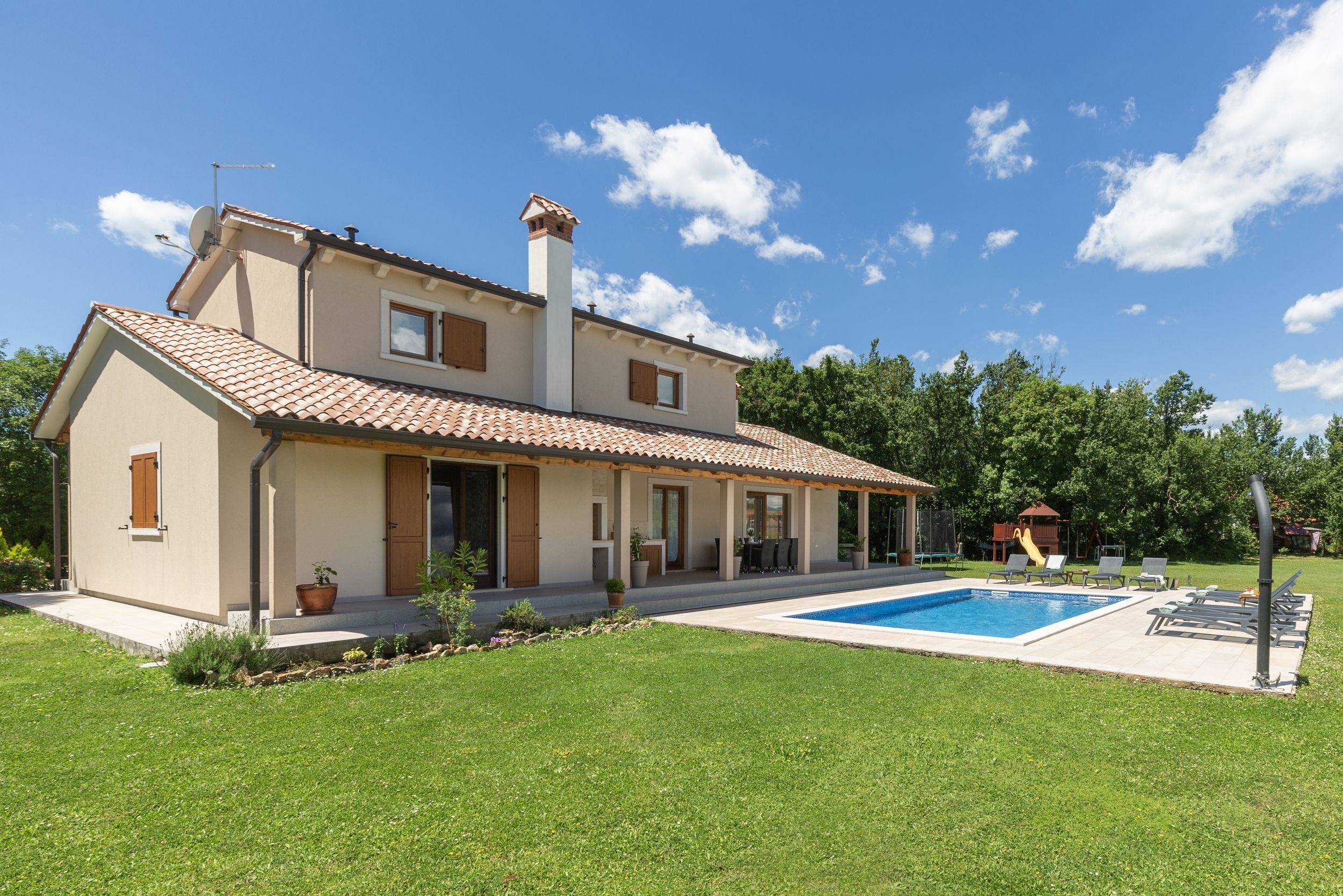 Uma casa de dois andares com piscina, varanda coberta e jardim.