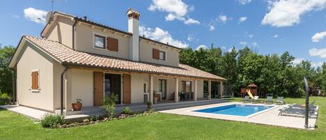 A two-story house with a swimming pool, a covered patio, and a garden.
