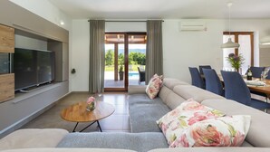 Uma sala de estar moderna com um sofá, uma televisão e uma área de jantar com cadeiras e uma mesa.