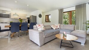 Uma sala de estar moderna com sofá, cadeiras, uma mesa de centro e uma área de cozinha ao fundo.