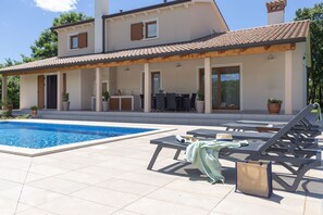 Una casa moderna con piscina, mobiliario de exterior y un porche cubierto.