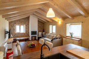 Ein gemütlicher Loft-Wohnraum mit Steinwand, Holzbalken, einem Essbereich mit Obstschale und einer Küchenzeile.