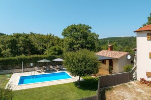 Uma propriedade residencial com piscina, pátio de pedra e vista para uma encosta arborizada.