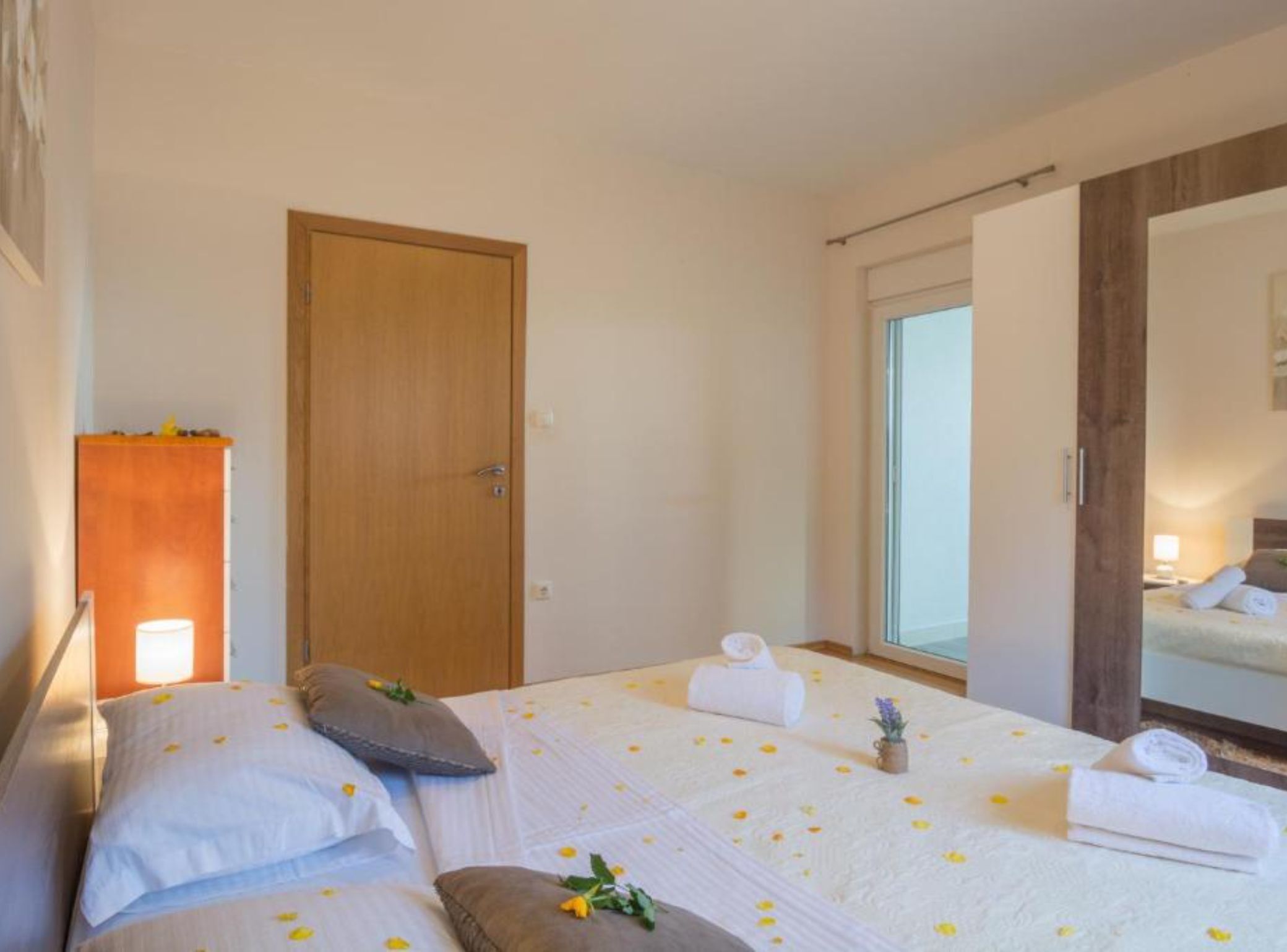 Una habitación de hotel con una cama, una puerta de madera, una ventana y un espejo.