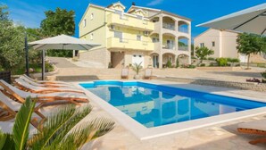 A poolside area with lounge chairs and a swimming pool, surrounded by a large building with multiple balconies and a garden. - Holiday House Balen With Swimming Pool (Benkovac)